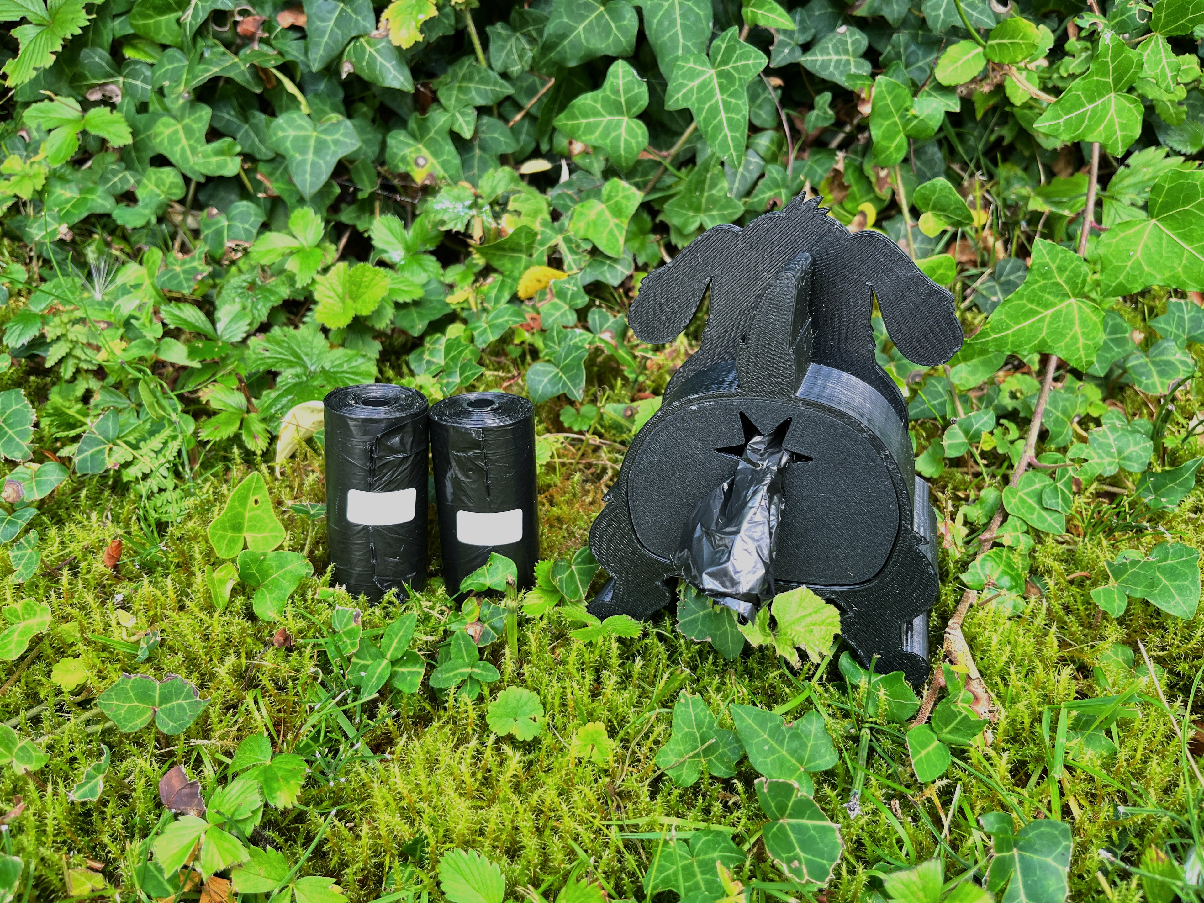Schwarzer Shitting Dog Kotbeutelspender in Hundeform mit zwei Beutelrollen daneben